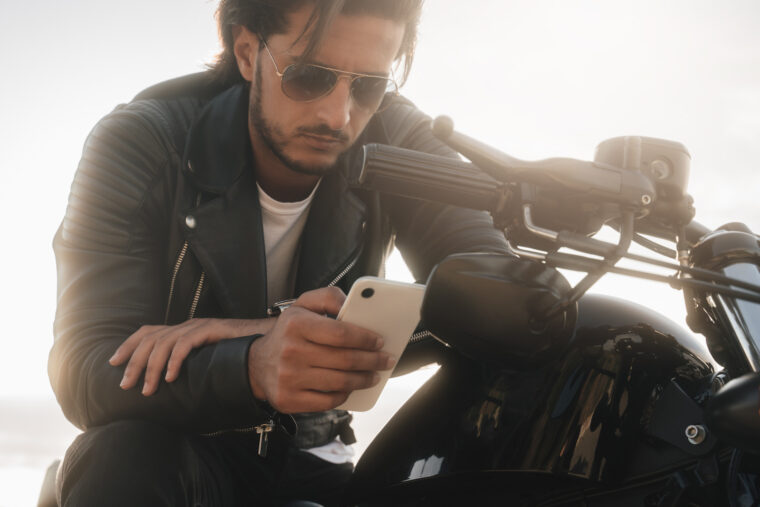 バイク上で携帯を手に悩む男性の画像
